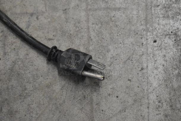 A black power cord plug from the Crathco D25-3 beverage machine, showing signs of use on a concrete surface.