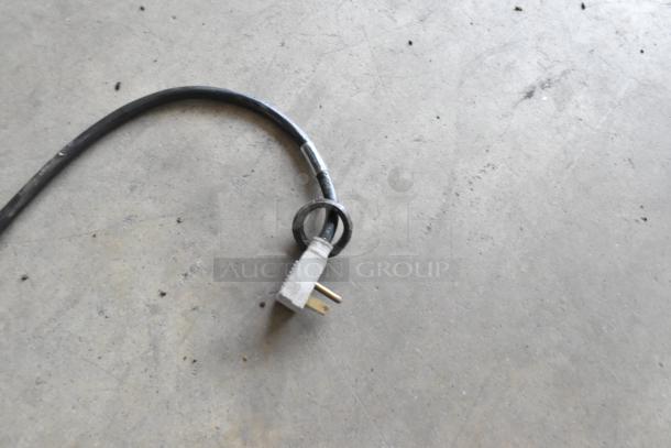 Power cord for a 2019 True ZGDM-36SL-HC-LD 2 Door Reach In Cooler. Black cable with standard plug, coiled on concrete floor.