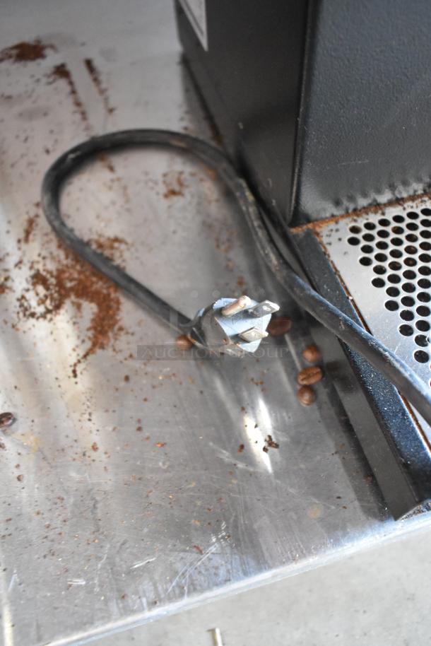 Bunn metal commercial countertop coffee bean grinder, 120 volts, 1 phase, shown with power cord and coffee grounds visible nearby.