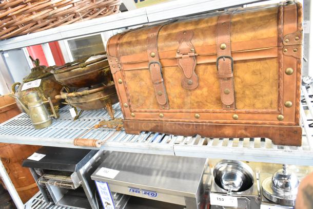 Wooden chest with leather straps and brass accents, alongside vintage brass bowls and decorative items on shelves.