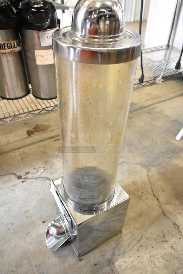 Clear metal dry dispenser with chrome accents, visible wear and residue inside, suitable for kitchen or commercial use.