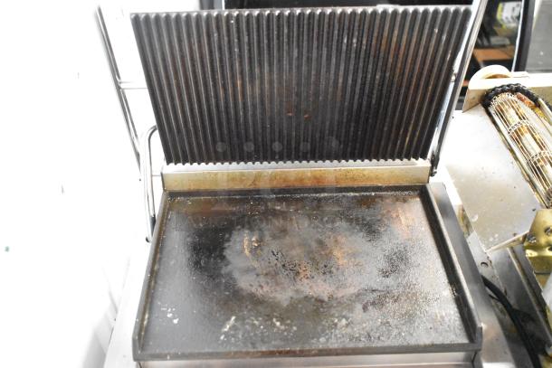 Commercial stainless steel panini press, model TCG-511EC. Features ridged top plate, worn cooking surface. 110V, 1 phase.