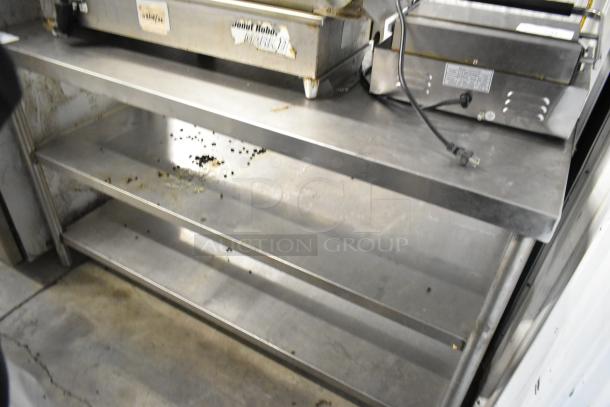 Stainless steel table with two under shelves, showing signs of wear. Ideal for kitchen or workshop storage.