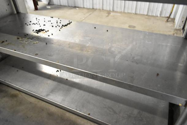 Stainless steel table with two under shelves, visible wear, minor surface residue. Ideal for kitchens or workshops.