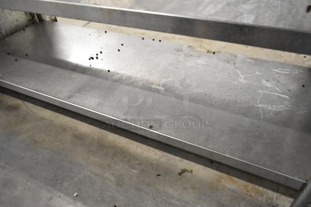 Stainless steel table with two under shelves, visible wear and minor surface debris. Ideal for heavy-duty use.