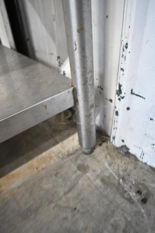 Stainless steel table corner with leg and lower shelf, showing signs of wear and surface marks.