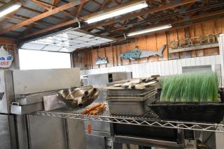 Tiered lot with stainless steel drop-in bins, assorted utensils, and fake grass on a metal shelf in a warehouse.
