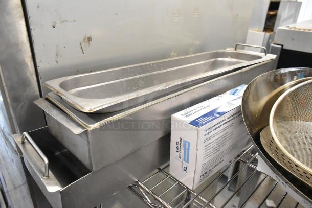 Stainless steel drop-in bins with handles, vinyl glove box, and a metal strainer on a wire shelf, in used condition.