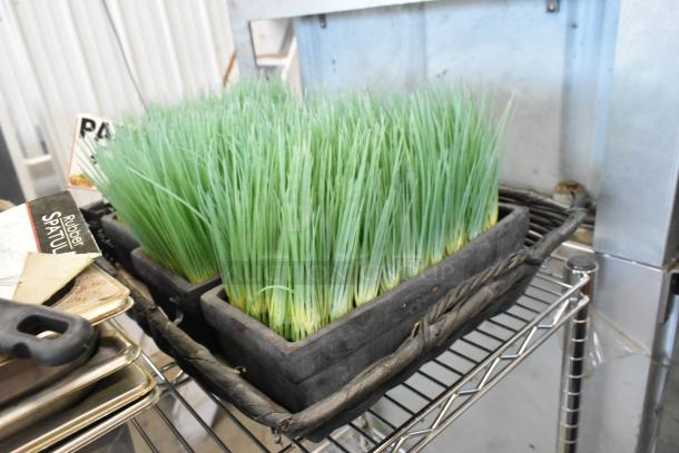 Tier lot including stainless steel drop-in bins, utensils with packaging, and potted fake grass on metal shelving.