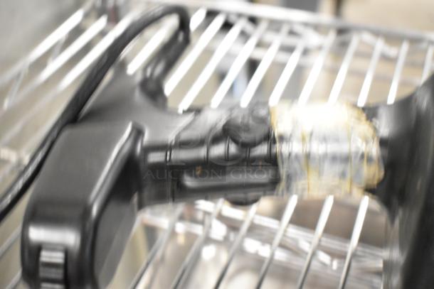 Blurry image of a Waring WSB Commercial Immersion Blender handle on a metal rack. No visible markings or labels.