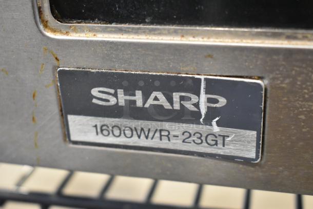 Sharp R-23GT-F stainless steel commercial microwave, 1600W, with label showing model and power specifications. Signs of wear present.
