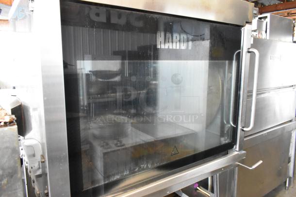 Hardt GC/4000 stainless steel commercial gas rotisserie oven, with glass front, on metal legs with casters. Visible Hardt logo.
