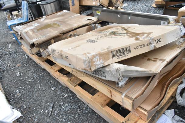 Packages of Lancaster Table & Seating 36" Square Outdoor Tables with ornate legs, visible shipping wear. Model 427COSM3636G.