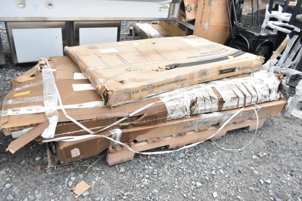 Packages containing scratch and dent stainless steel table, black outdoor table, and chair frames on a pallet. Boxes show wear.