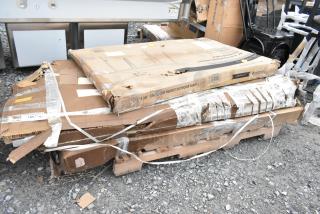 Packages containing scratch and dent stainless steel table, black outdoor table, and chair frames on a pallet. Boxes show wear.