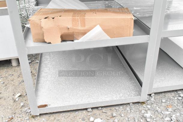 Gray metal 3-tier cart, brand new with scratch and dent. Cardboard packaging visible. Ideal for storage or utility use.