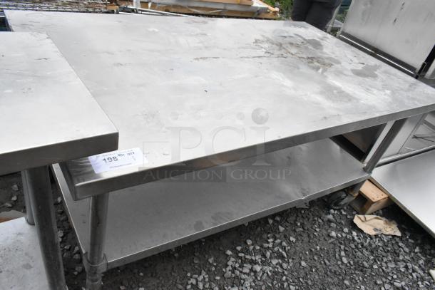 Stainless steel table with metal under shelf on commercial casters. Light surface wear visible. Auction tag on side.