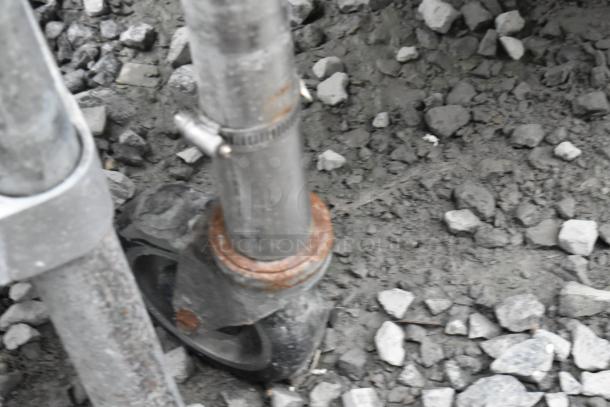 Stainless steel table leg with metal under shelf, mounted on commercial casters, shown on rocky ground.