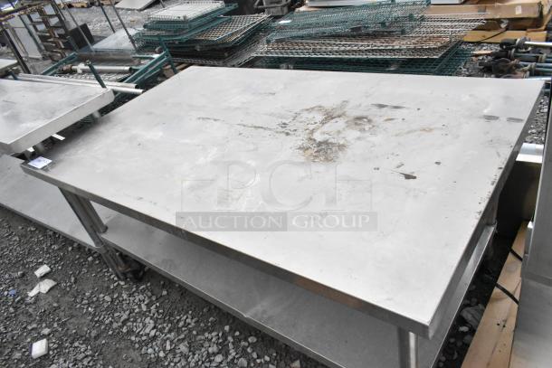 Stainless steel table with metal under shelf and commercial casters, showing signs of wear and surface marks.