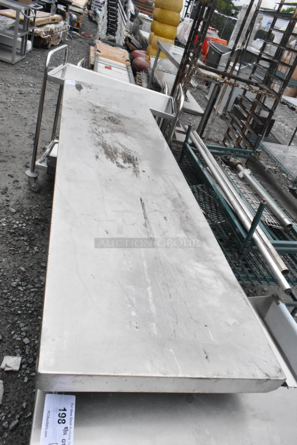 Stainless steel table with metal under shelf, shows wear and surface scratches. Auction tag visible with lot number 198.