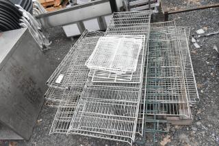 Lot of various wire shelves in mixed condition, stacked on gravel. Includes metal and coated shelves of different sizes.