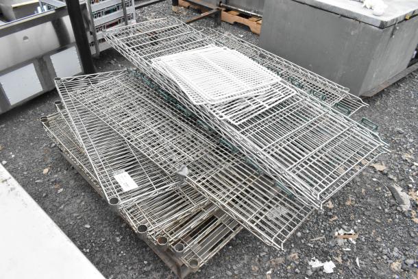 Various wire shelves in assorted sizes, stacked on a pallet. Some have green edges. One shelf has a visible label.