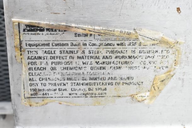 Metal tag on stainless steel table, indicating guarantee against defects. Eagle brand, cleaning instructions included.