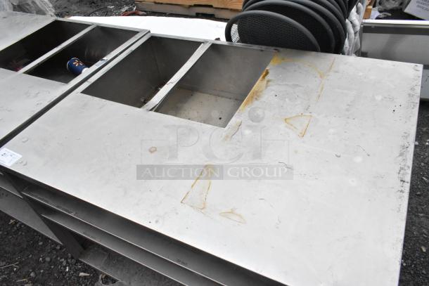 Stainless steel counter with cut out, featuring three under shelves. Shows signs of wear and rust marks. Auction tag attached.