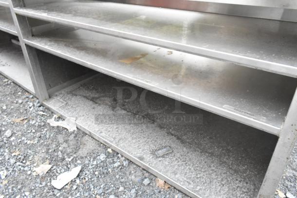 Stainless steel counter with cutout, featuring 3 under shelves. Signs of wear and dust are visible. Suitable for kitchen use.