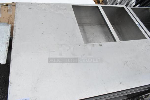 Stainless steel counter with cutout and three under shelves, showing minor surface marks, ideal for kitchen use.