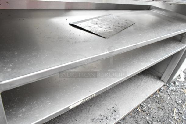 Stainless steel counter with cutout and three under shelves. Features durable construction, suitable for kitchen use. Some visible wear.