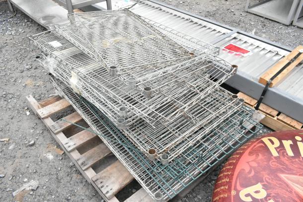 Lot of various metal wire shelves stacked on pallet, used condition, suitable for storage or retail use.