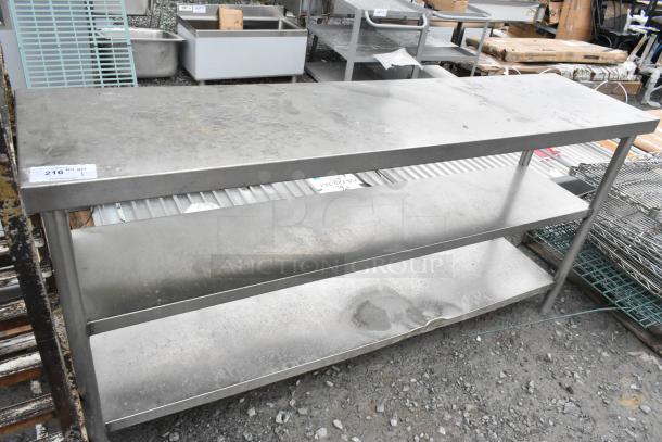 Stainless steel table with two under shelves, industrial setting, signs of wear, ideal for kitchen or workspace use.