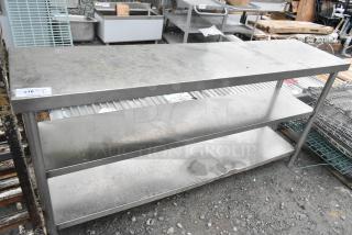 Stainless steel table with two under shelves, industrial setting, signs of wear, ideal for kitchen or workspace use.