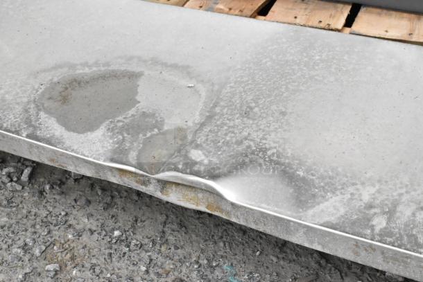Stainless steel table showing surface wear and dents, with two under shelves, suitable for heavy-duty use.