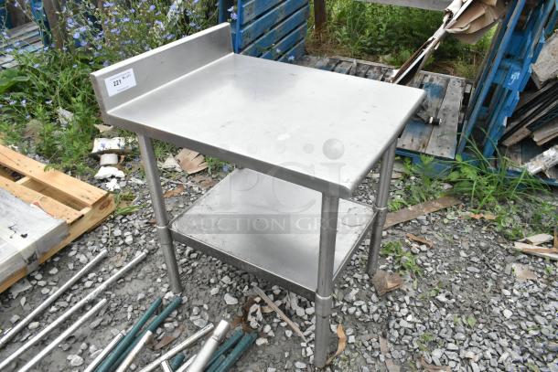 Stainless steel table with metal undershelf, shows signs of outdoor use, label "221 19 Qt" on splashback.