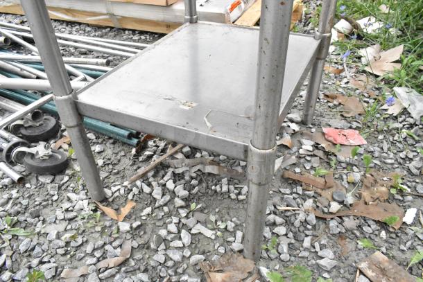 Stainless steel table with metal under shelf, featuring sturdy legs. Condition shows wear, suitable for industrial use.