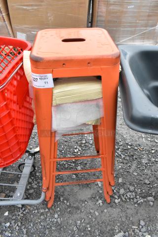 Three red Tolix style bar stools, new with minor scratches and dents. Includes label "227 x3". Stacked in outdoor setting.