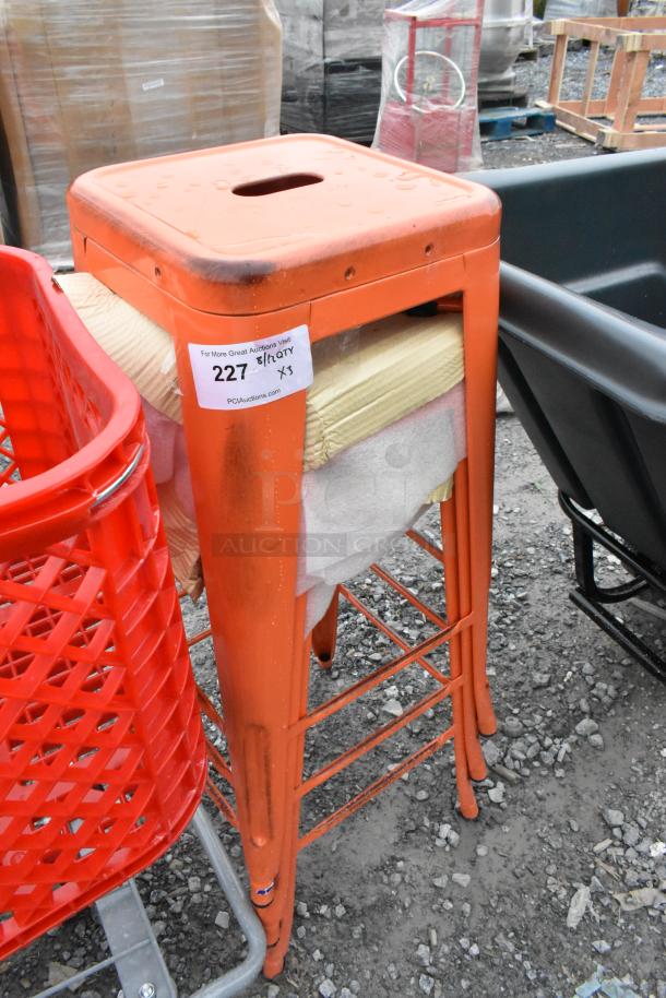 Three red metal Tolix style bar stools, new with scratch and dent marks, and auction label “227 x3.”