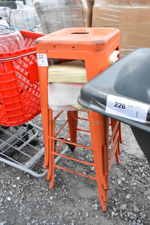 Three red metal Tolix-style bar stools, new with scratches and dents. Stacked display; auction tag visible.