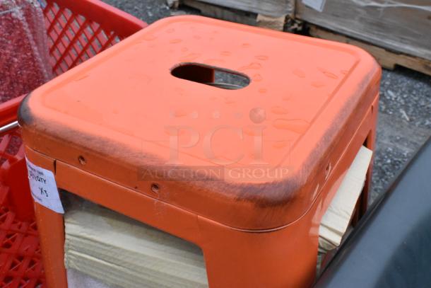 Three new red metal Tolix style bar stools with visible scratches and dents. Label indicates auction quantity x3.