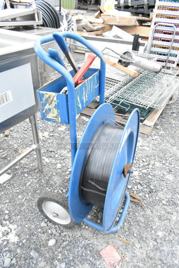 Blue metal pallet banding cart with contents, features large spool of strapping and two handles, used condition.