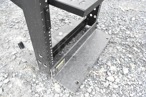 Black metal shelving unit with adjustable levels. Visible caution label. Slight wear. Perfect for garage or workshop use.