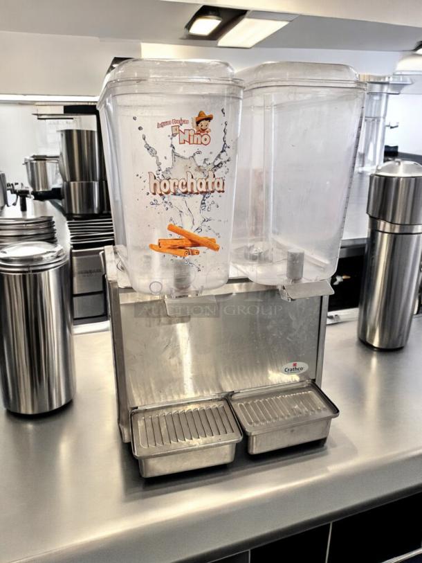 Crathco D25-3 dual bowl cold beverage dispenser, excellent condition, 115V, with one labeled "horchata," on a stainless steel countertop.