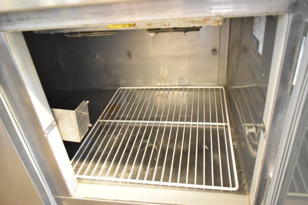 Stainless steel commercial pizza prep table with interior shelving, on casters, 115V, 1 Phase. Slight wear visible.