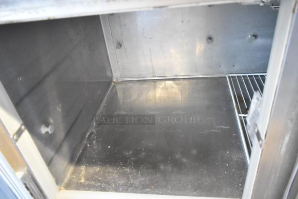 Stainless steel commercial pizza prep table, interior view. Features shelving and spacious design. 115 volts, 1 phase.