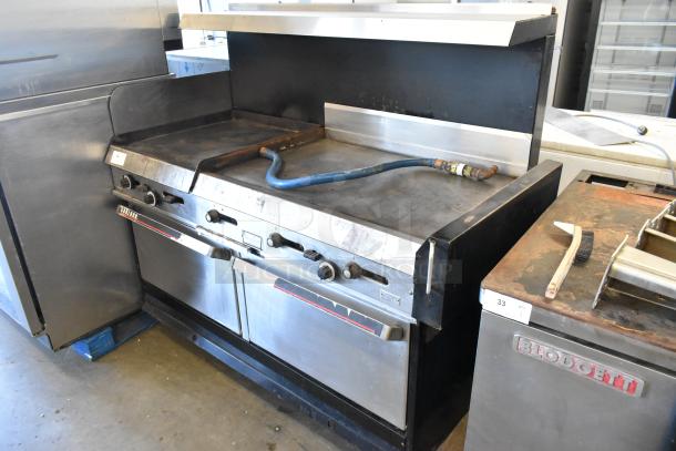 Garland commercial gas griddle with 2 ovens, flat top, over shelf, and backsplash. Used condition with visible controls and blue hose.