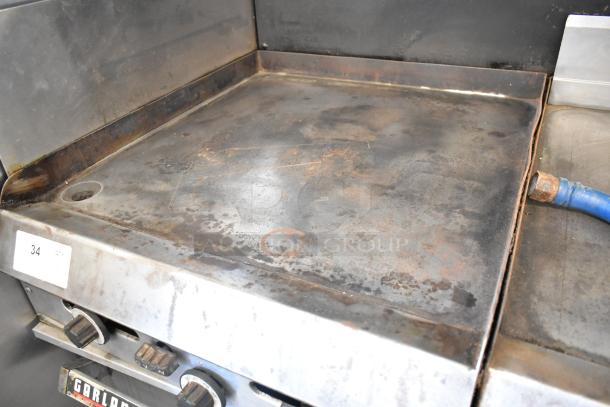 Garland commercial 2-section gas griddle with dual ovens, overshelf, and backsplash. Some surface wear, durable metal build.