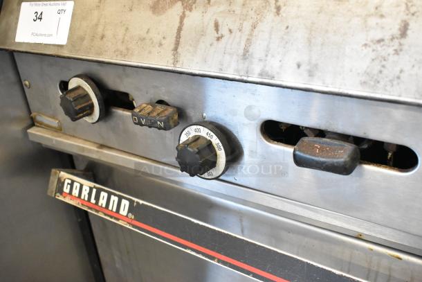 Garland metal commercial gas griddle with two ovens, control knobs, over shelf, and backsplash, used condition.