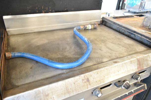 Garland commercial gas flat top griddle with two ovens, over shelf, and back splash. Features a metal finish and blue gas line.